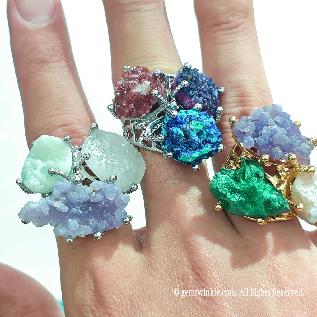 Hand holding and wearing multiple raw crystal trio claw rings showcasing unique gemstone rough combinations and claw mountings