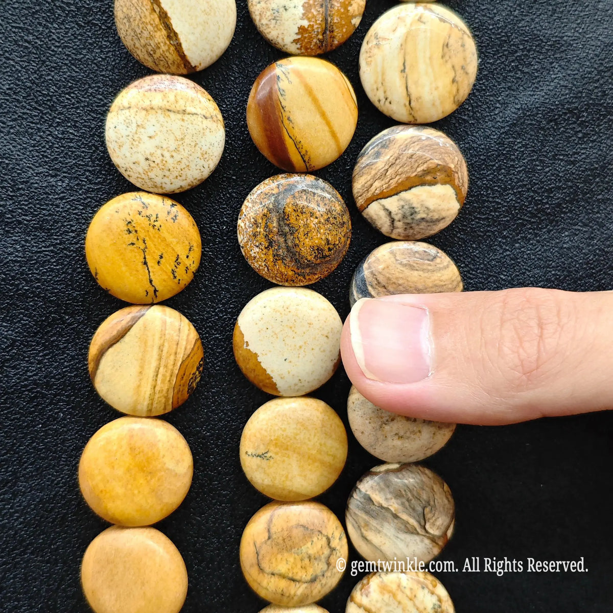 Finger pointing to a smooth flat round picture jasper coin bead displaying earthy brown and cream landscape lines