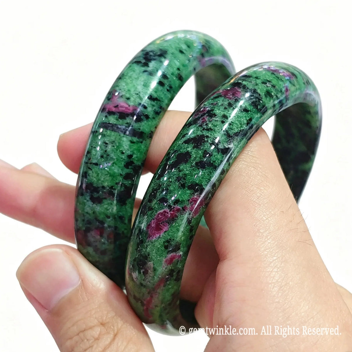Stacked natural ruby in zoisite gemstone bangles resting on palm displaying classic circular shape and vibrant colors