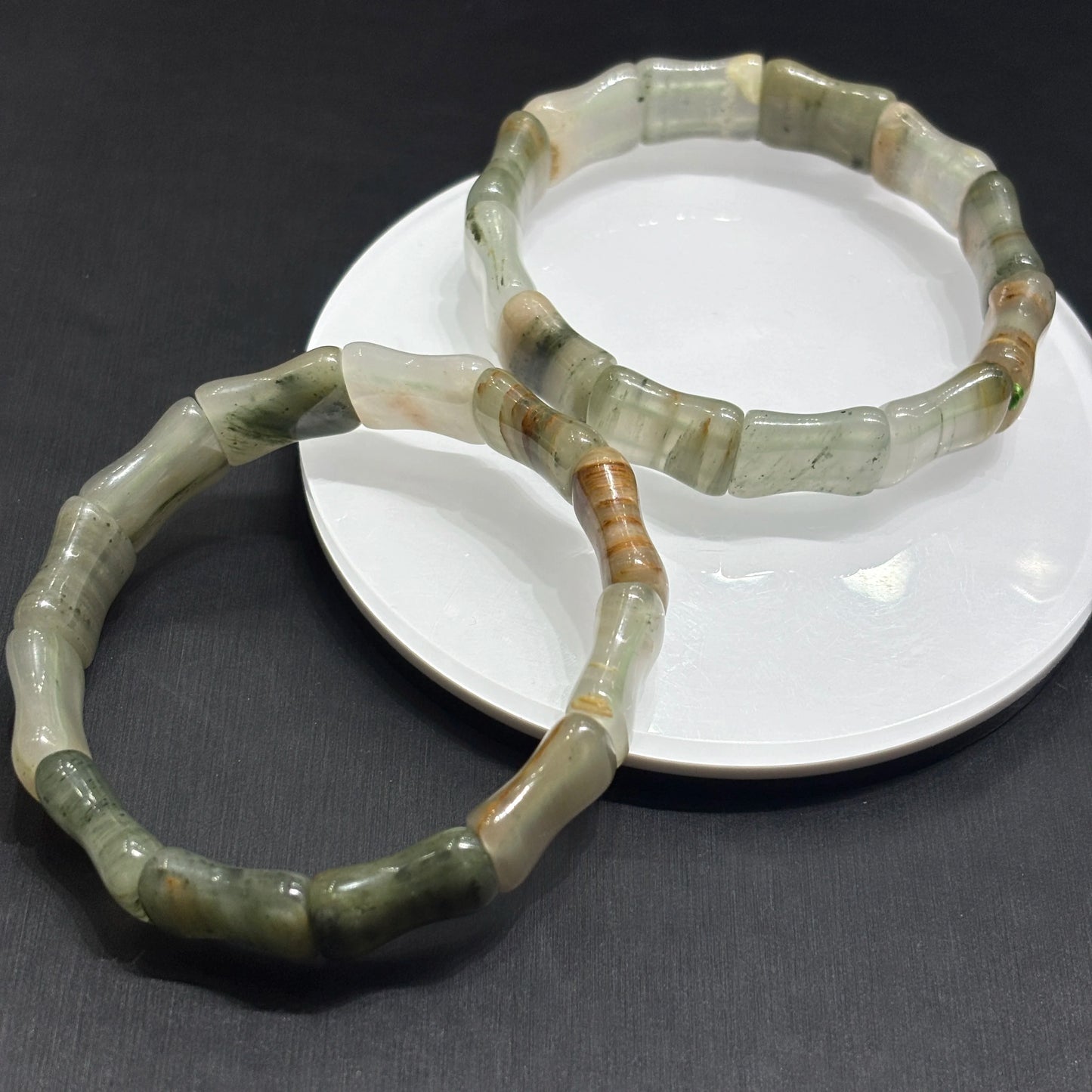 Two green jade bracelets on a white dish against a dark background