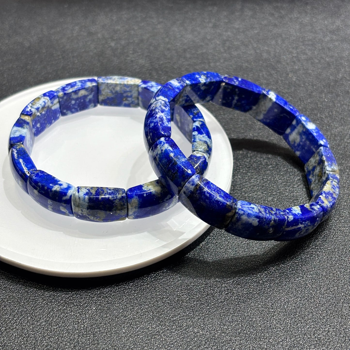 Two lapis lazuli square bead bracelets layered on ceramic plate; deep blue with white veins, perfect for boho aesthetic layering