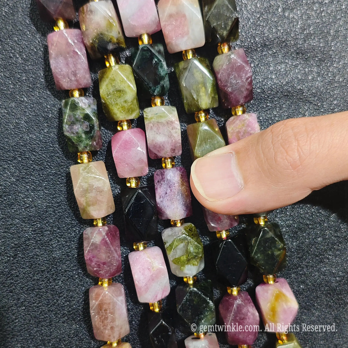 Hand displaying natural rainbow tourmaline faceted freeform beads showing rich candy tones and pre-drilled holes