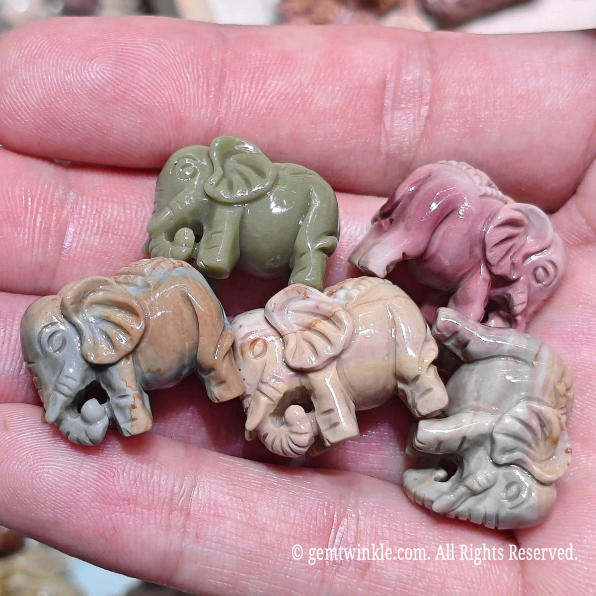 Hand holding six natural Alxa agate mini elephant carvings in various earth tones showcasing stable base and ear details