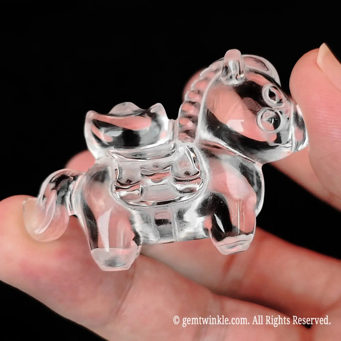Mini precision carved clear quartz horse carrying an ingot displayed on open fingers for accurate size scale reference