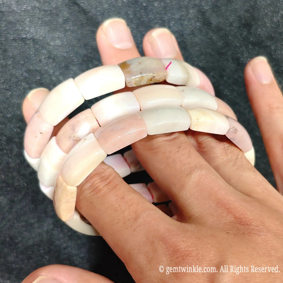 Close up view of stacked pastel pink opal smooth curved segment bracelets worn on hand showcasing blush pink and rose white tones