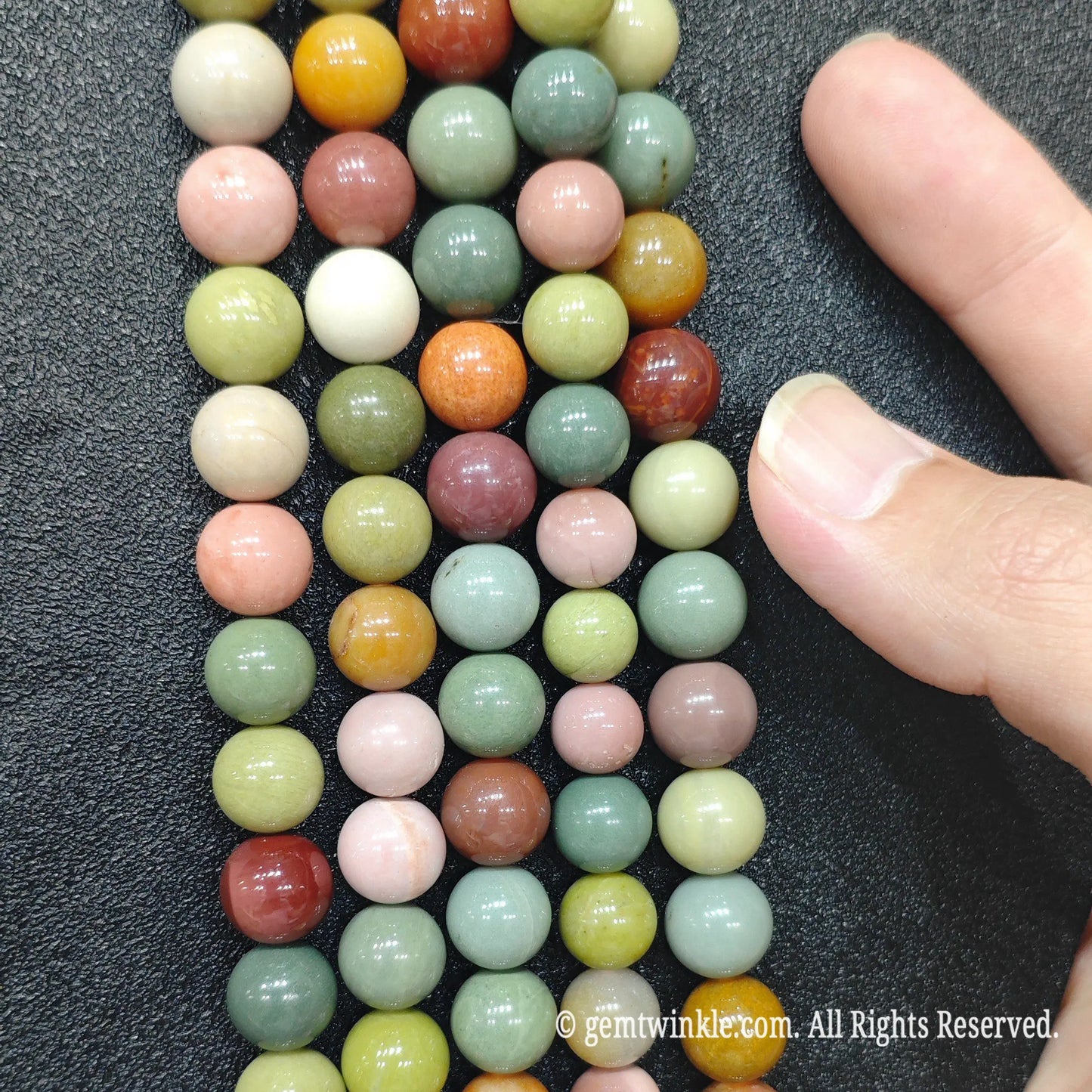 Finger pointing to natural multicolor Alashan Gobi agate round beads on strands for size reference and inspection