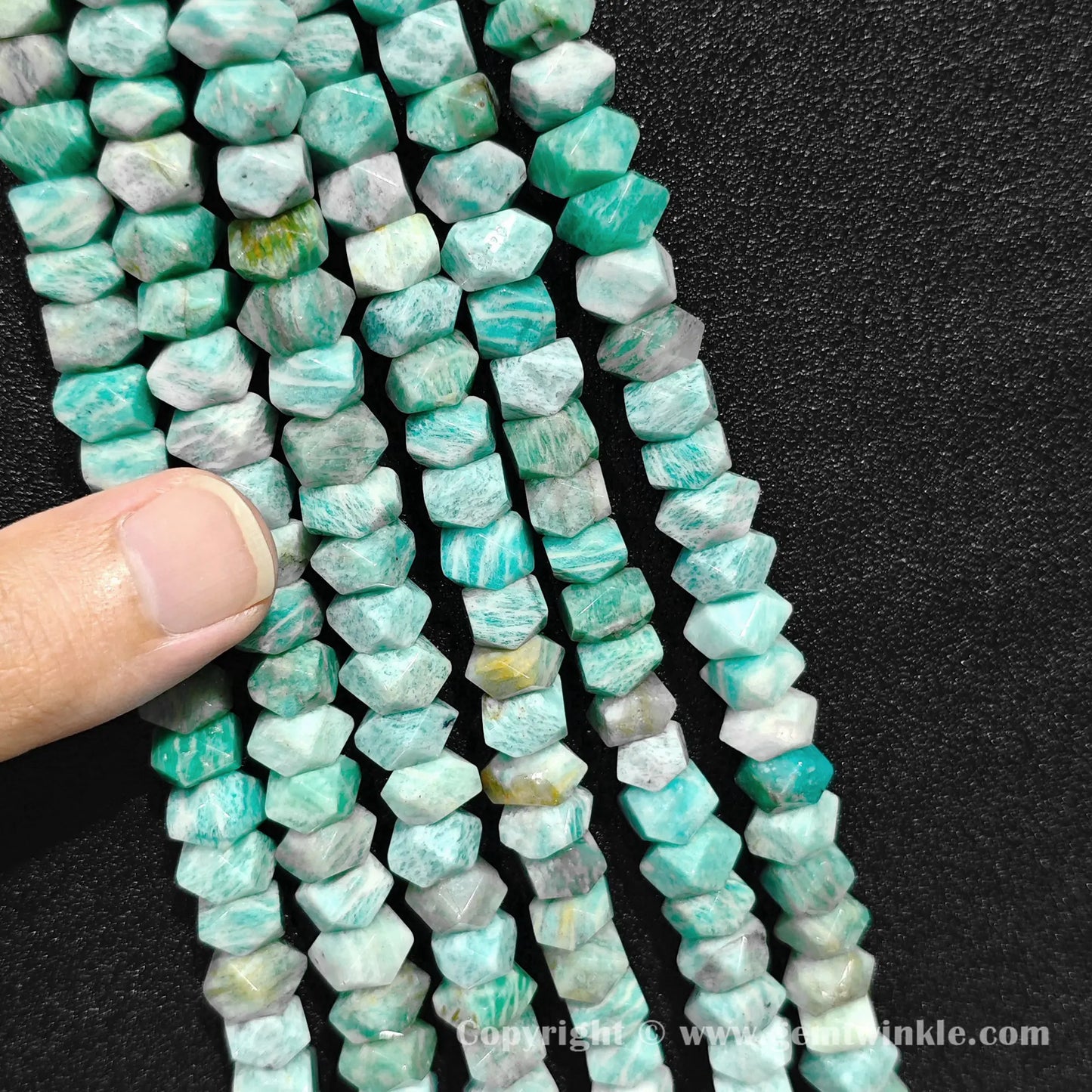 Hand holding multiple strands of natural amazonite 10x6mm faceted cylinder beads