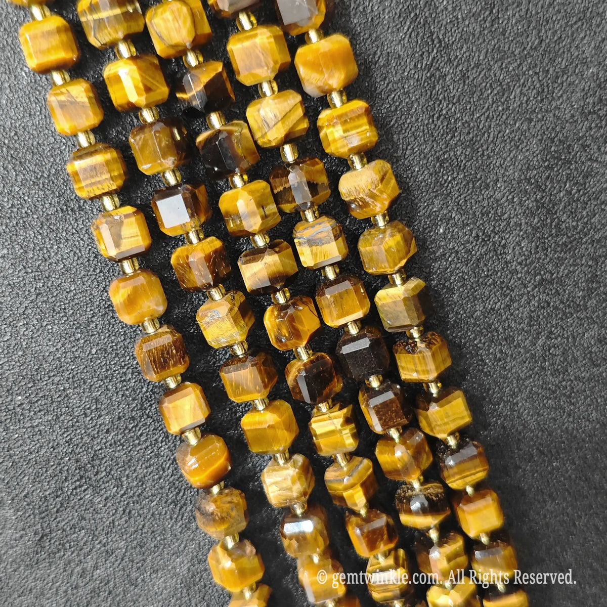 Designer hand holding golden tiger eye gemstone strands to demonstrate bead scale and polished luster
