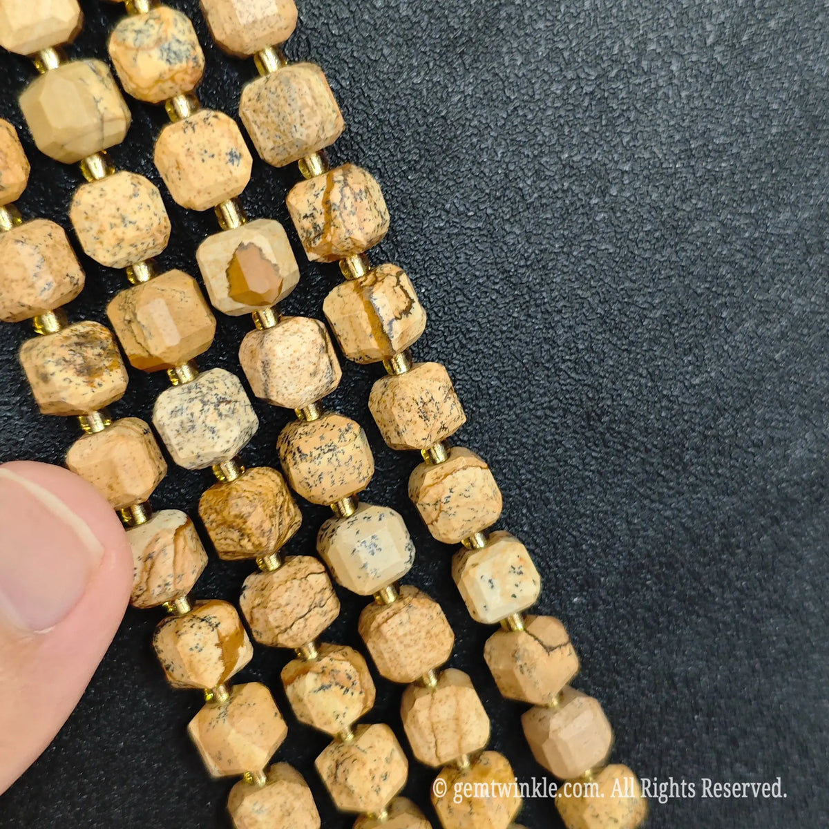 Designer hand holding wood grain stone gemstone strands to demonstrate bead scale and polished luster