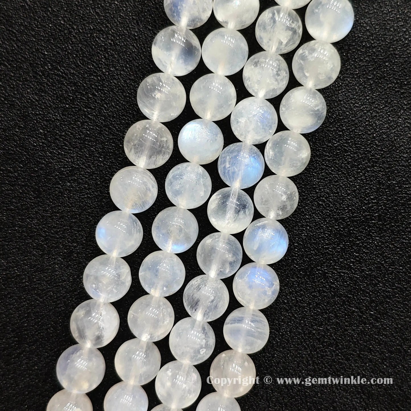Close up view of ice fractured blue flash moonstone round beads held on fingers for natural optical preview