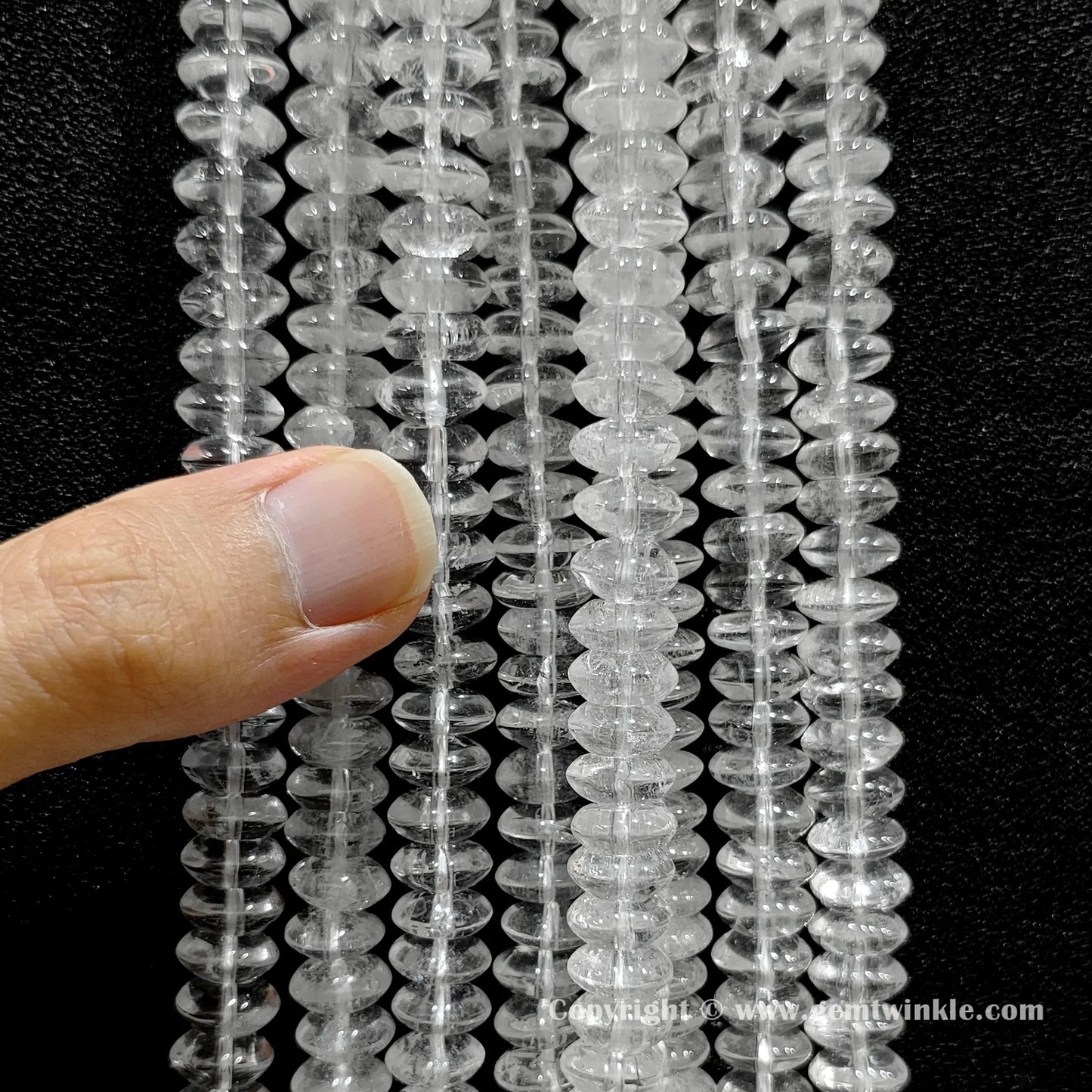 Close up view of natural clear quartz disc beads held on fingers for quality preview