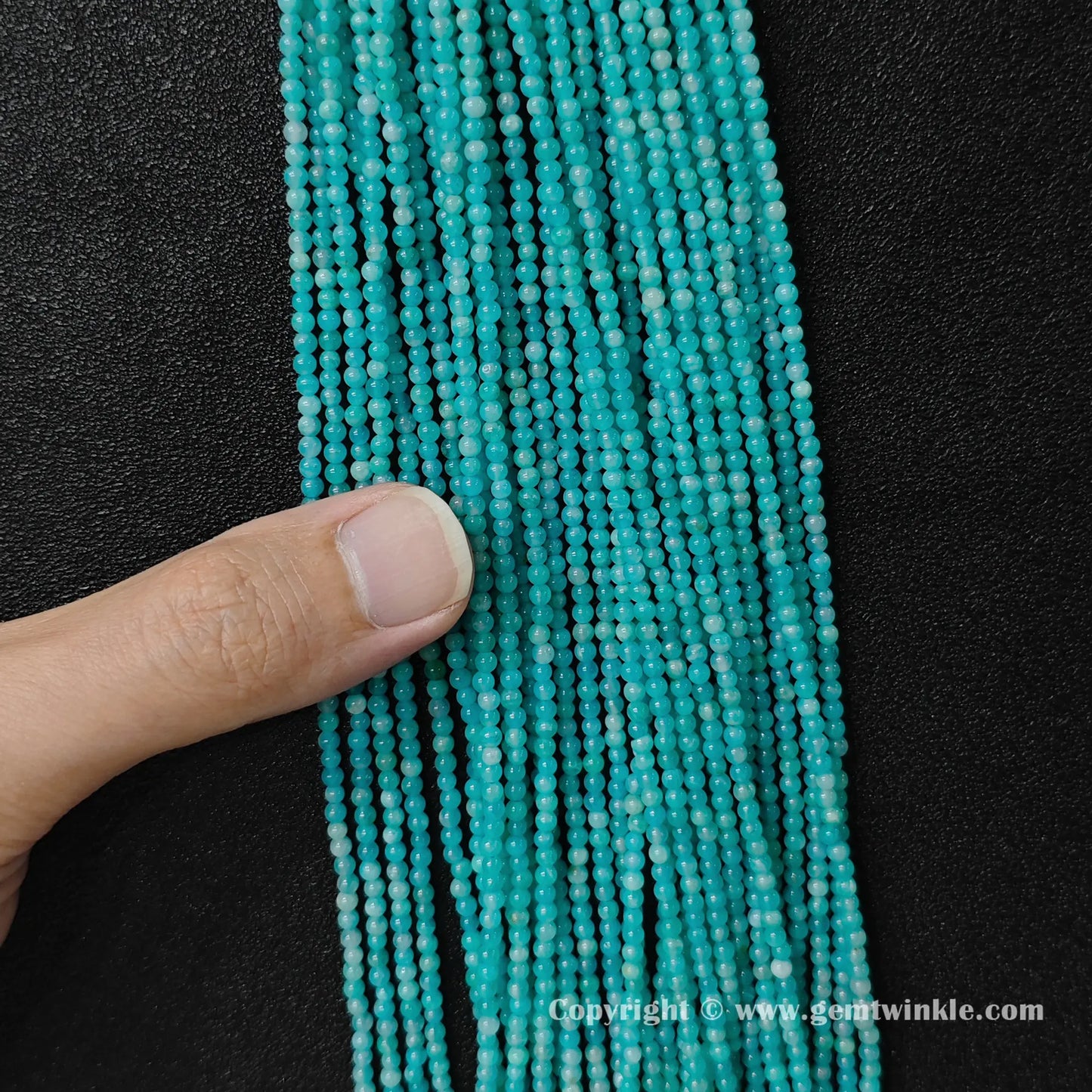 Hand holding delicate natural amazonite 3mm micro seed bead strands to demonstrate size scale and vivid luster