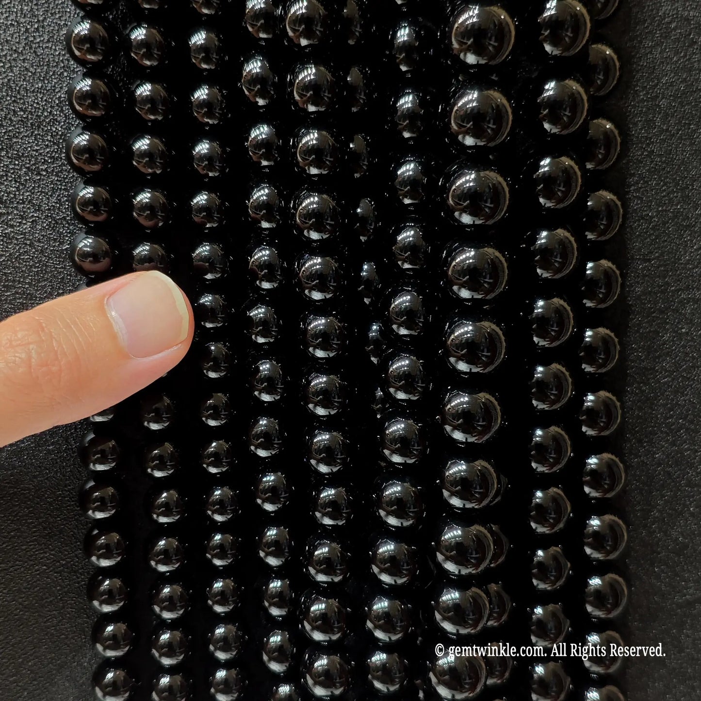 Hand holding black agate beads for scale and texture check