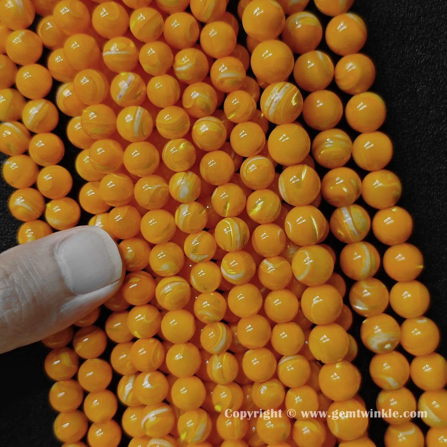 Finger holding dyed yellow mother of pearl bead strands demonstrating scale for jewelry supply