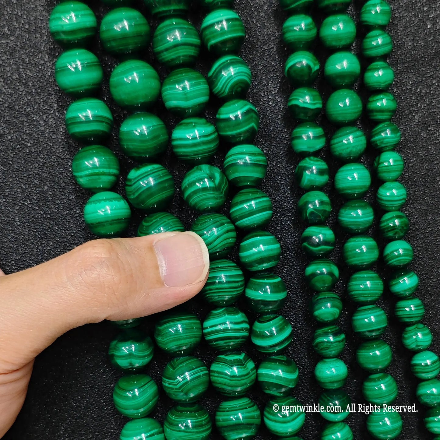 Round green malachite beads in progressive four to fourteen millimeter sizes held by hand to inspect scale and polish