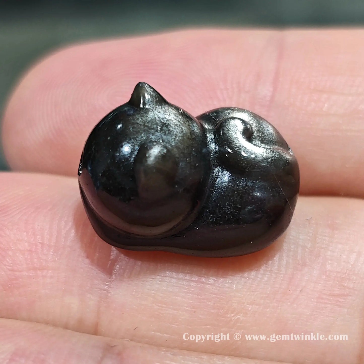 Back view of genuine silver sheen obsidian sleeping cat charm bead showing size proportions on fingers