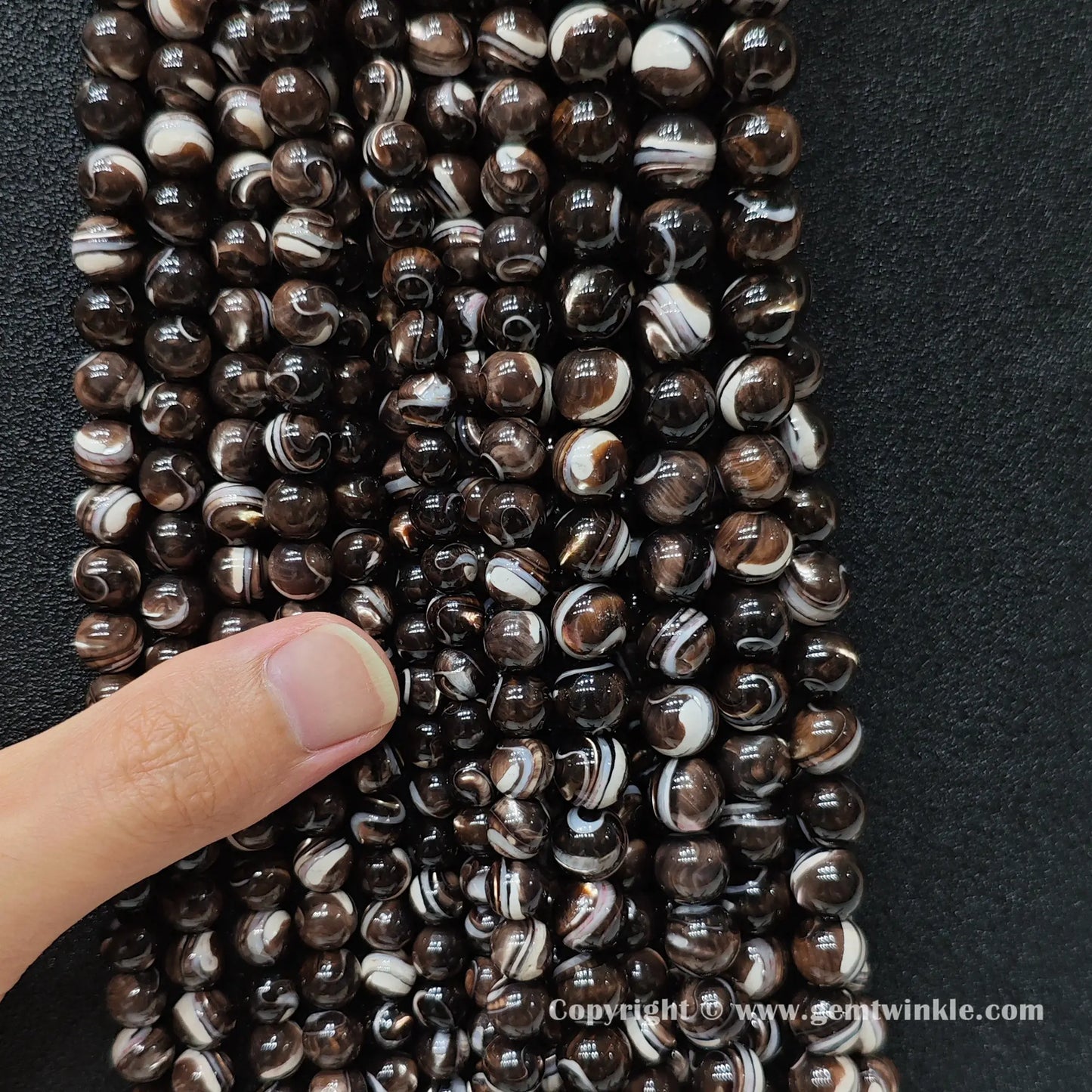 Hand holding natural grey mother of pearl bead strands demonstrating scale for jewelry supply