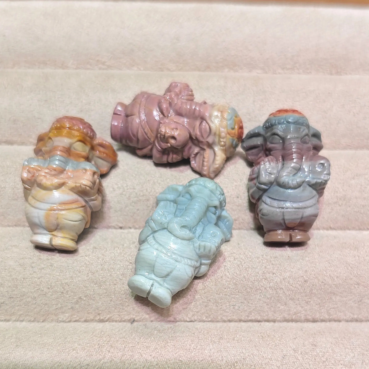 group display of multiple mini ganesha elephant god statues resting on display tray in various natural stone colors