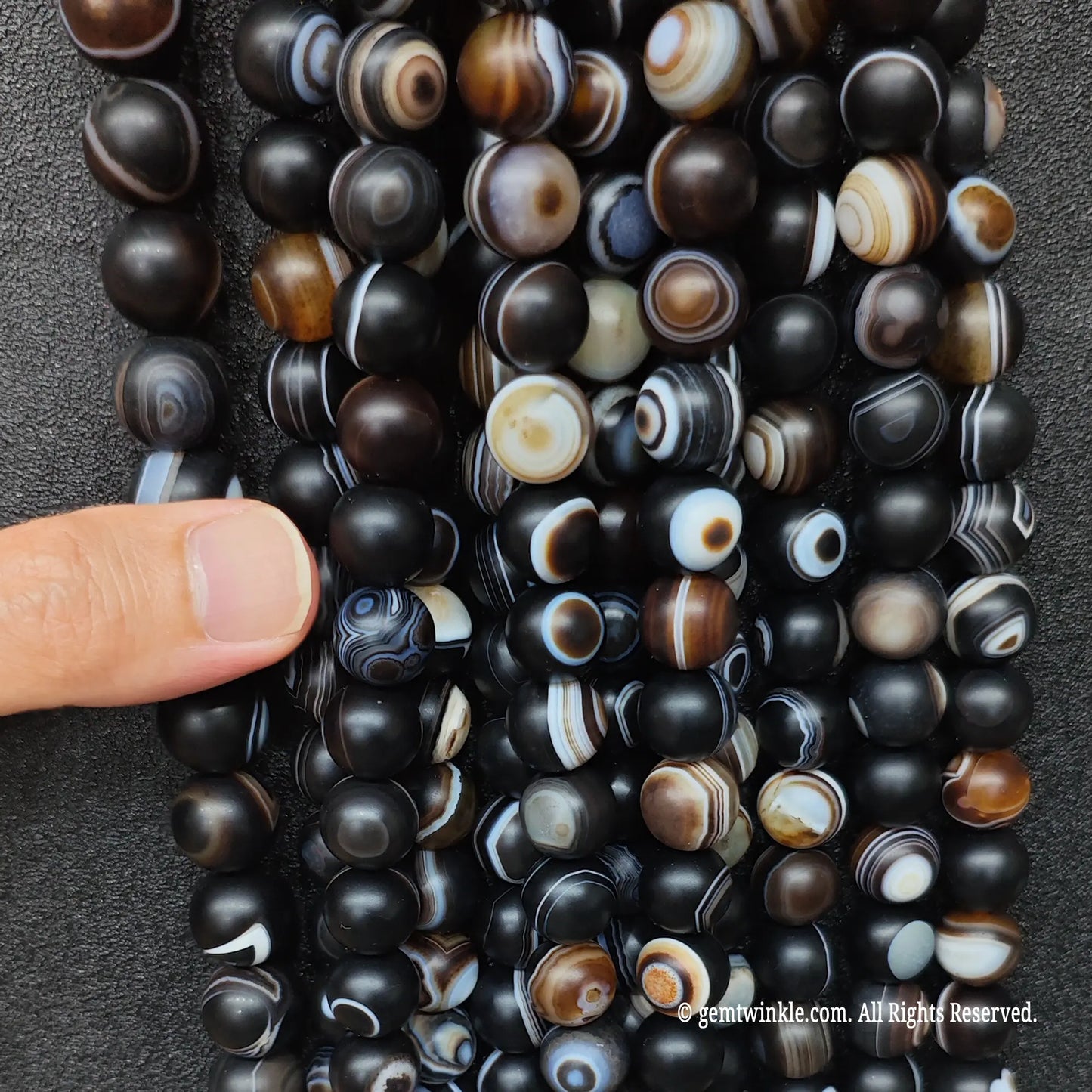 hand holding a large wholesale bundle of high quality gemstone beads in frosted black eye agate for boutique store sourcing