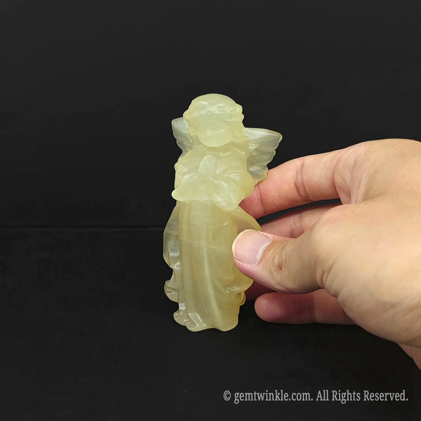 Hand holding an approx 10cm natural yellow calcite guardian angel carving to display actual physical size and waxy luster for crystal wholesale buyers