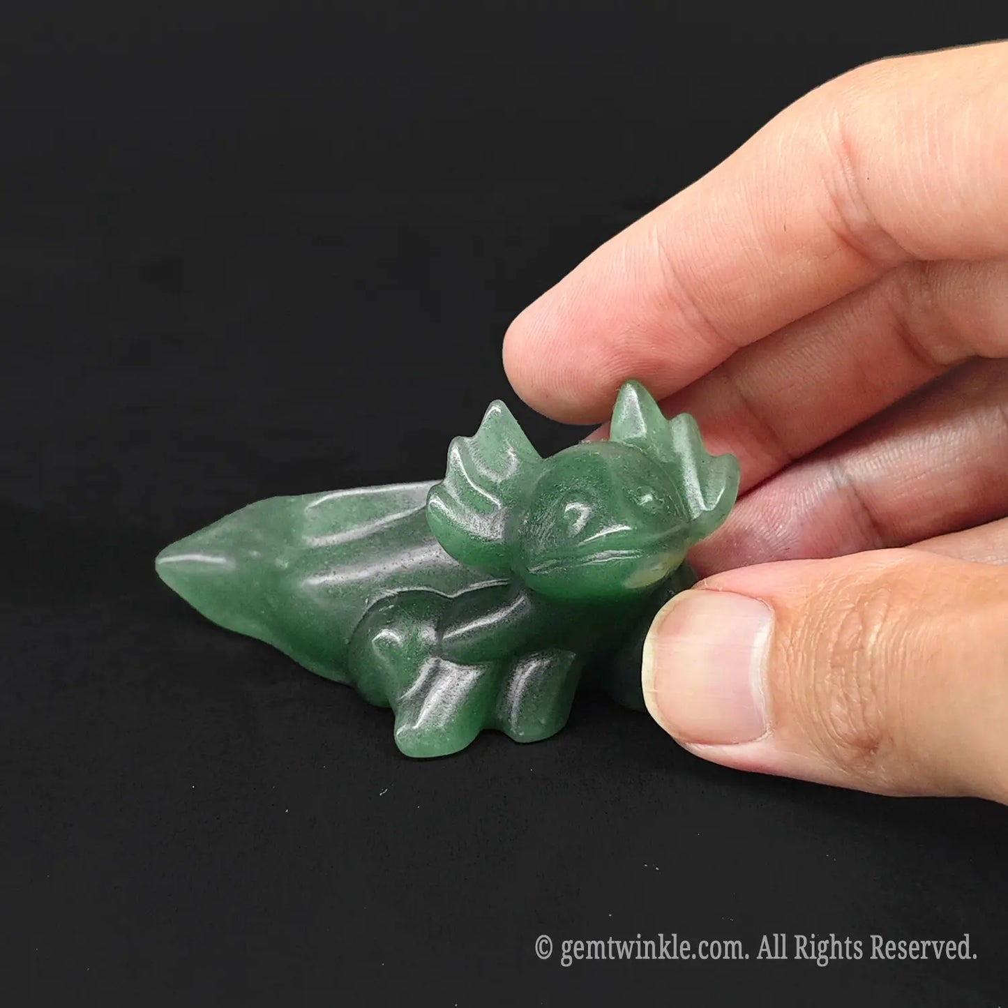 Hand holding a three inch green aventurine axolotl pocket stone showing physical scale and raw jade green coloration