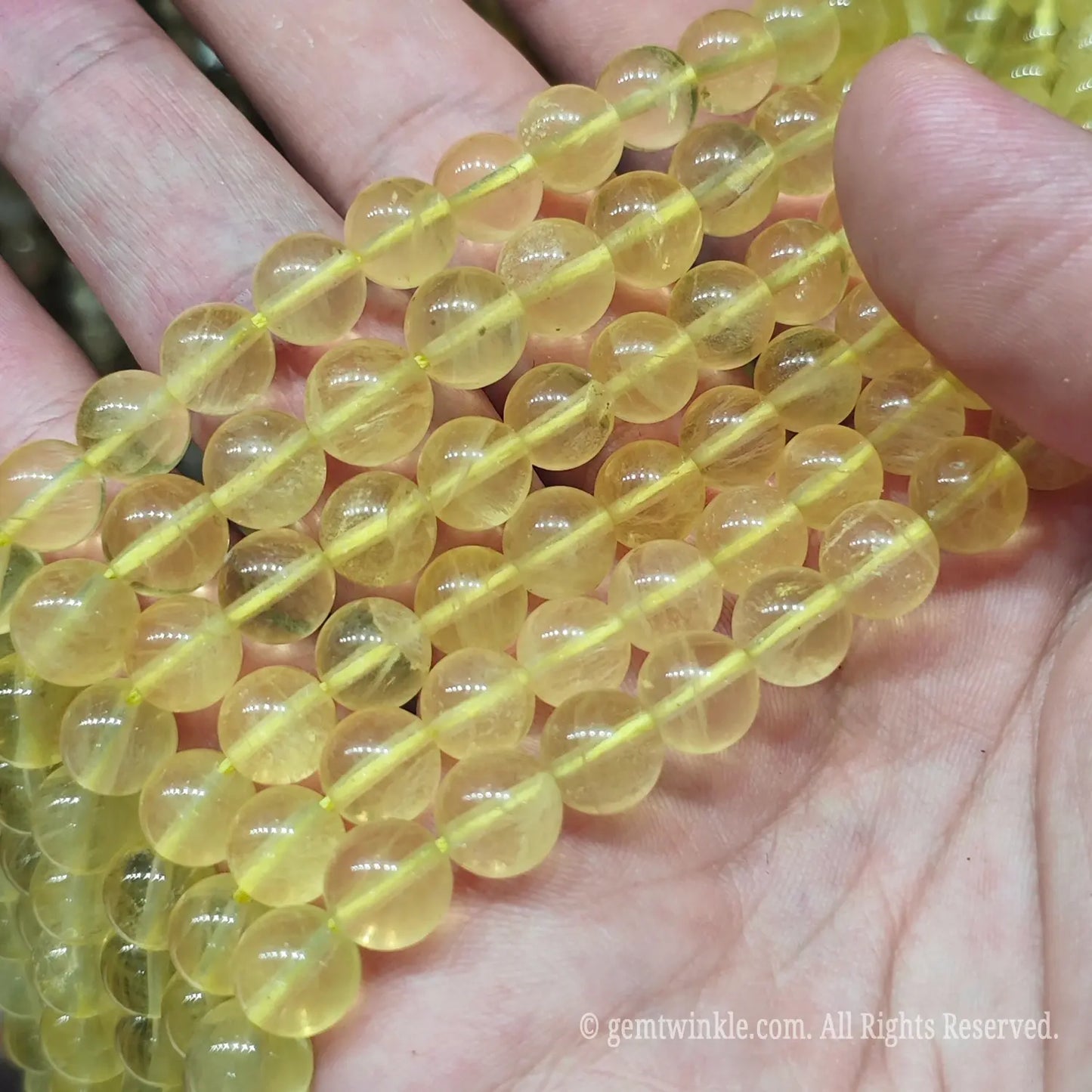 Hand holding translucent golden yellow fluorite loose beads strands under warm light for boutique jewelry designers and Etsy creators.
