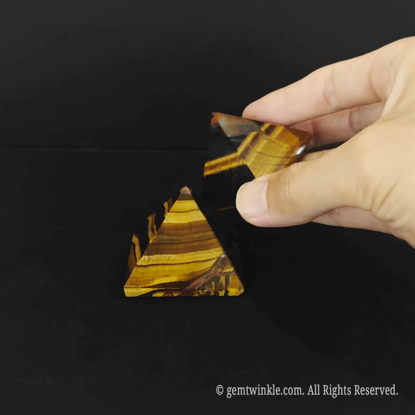 A hand removing the top segment of a layered gold tigers eye pyramid to reveal its internal joints