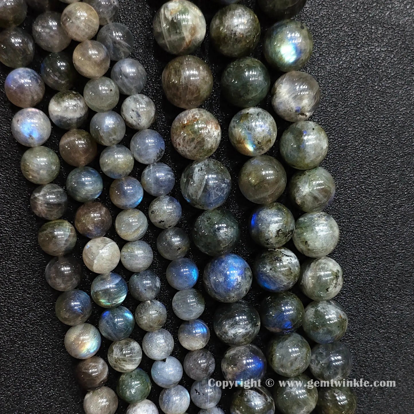 Full display of 8mm to 14mm natural grey moonstone gemstone strands laid flat on textured black leather surface