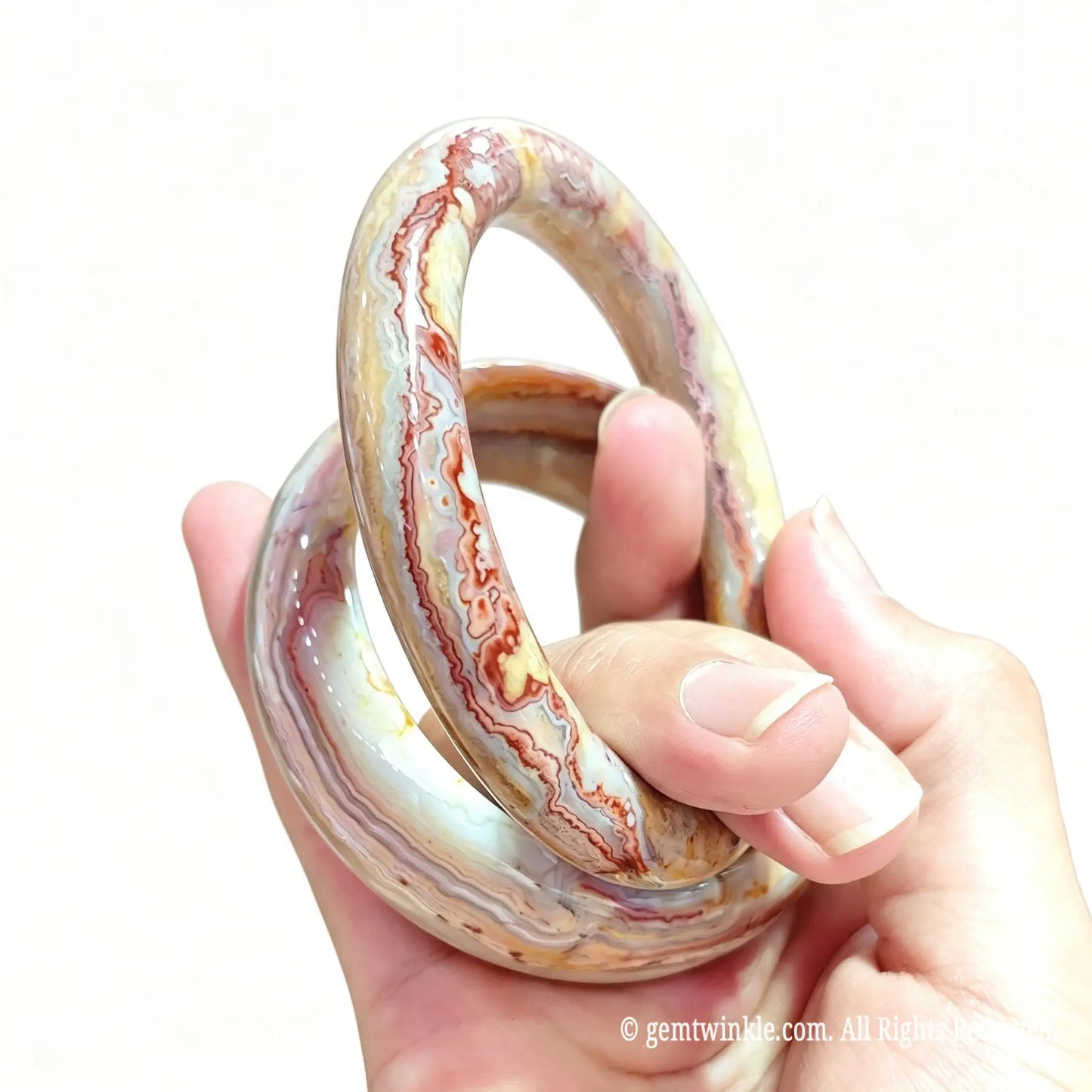 Side view of natural crazy lace agate bangles held in hand highlighting smooth edge finish