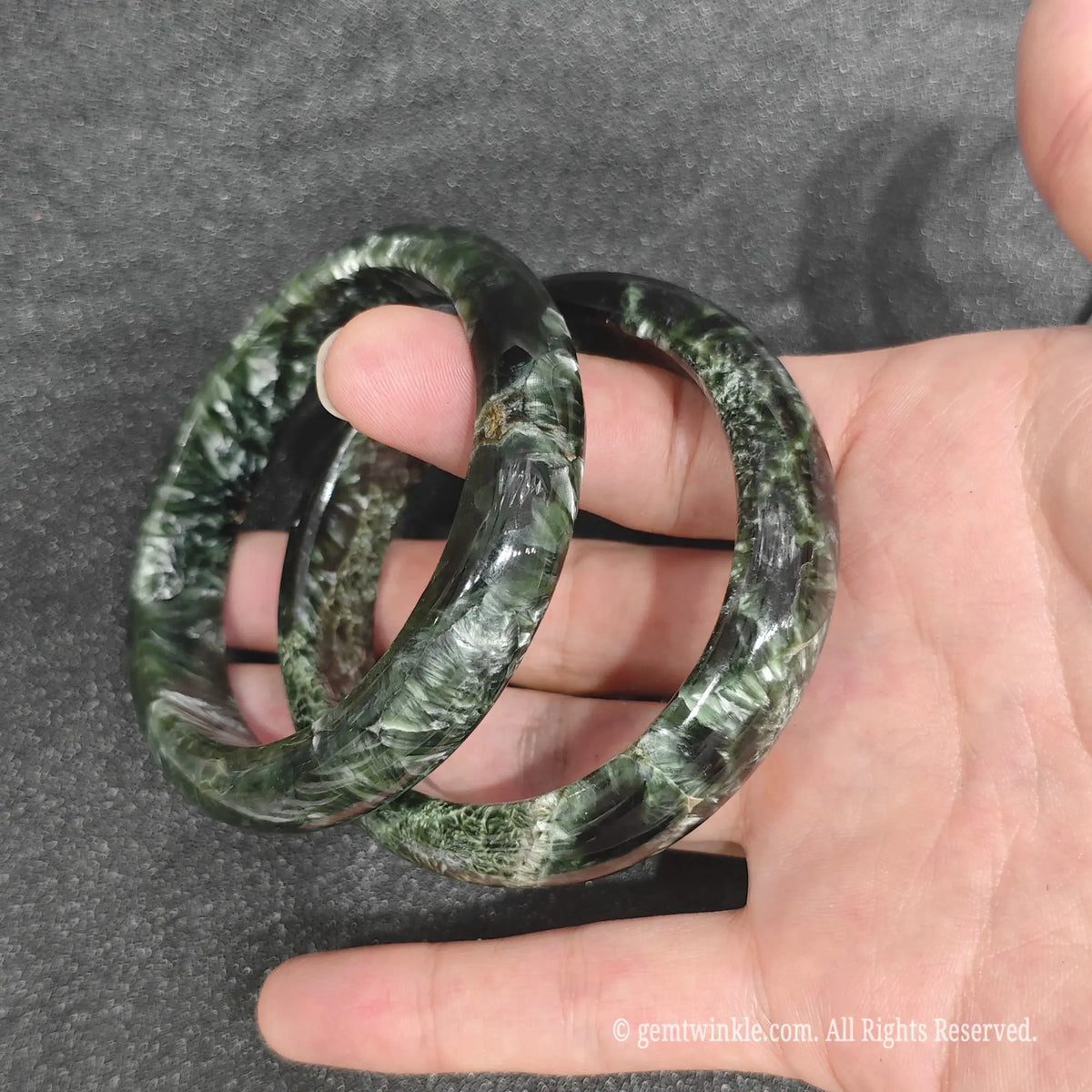 natural serafinite clinochlore gemstone bangle held in palm showing glossy finish and distinct feather matrix