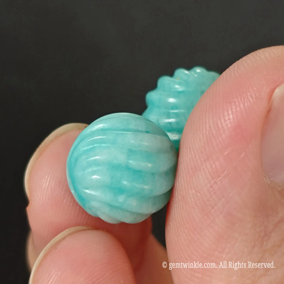 Amazonite carved threaded beads pair held between fingers showing side angle view and smooth glossy finish