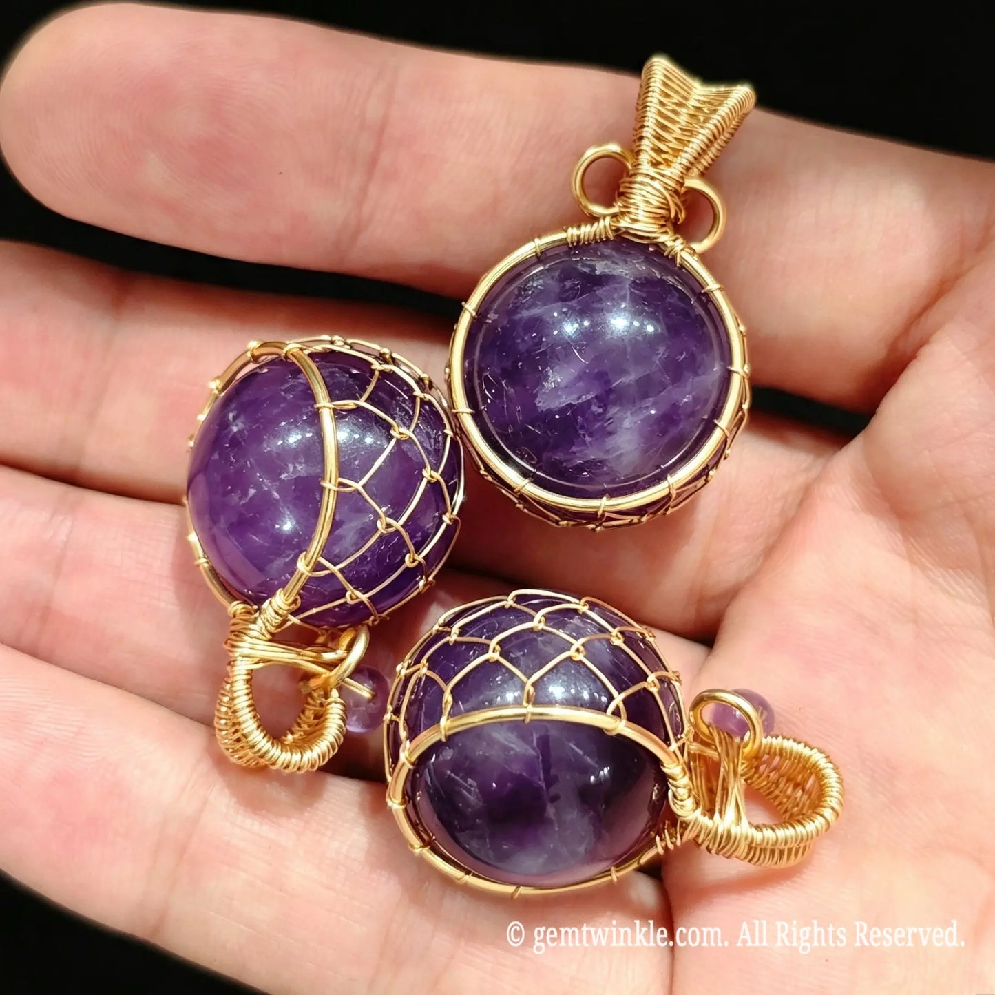 Group view of 20mm amethyst sphere pendants held in hand highlighting gold wire cage design for jewelry making