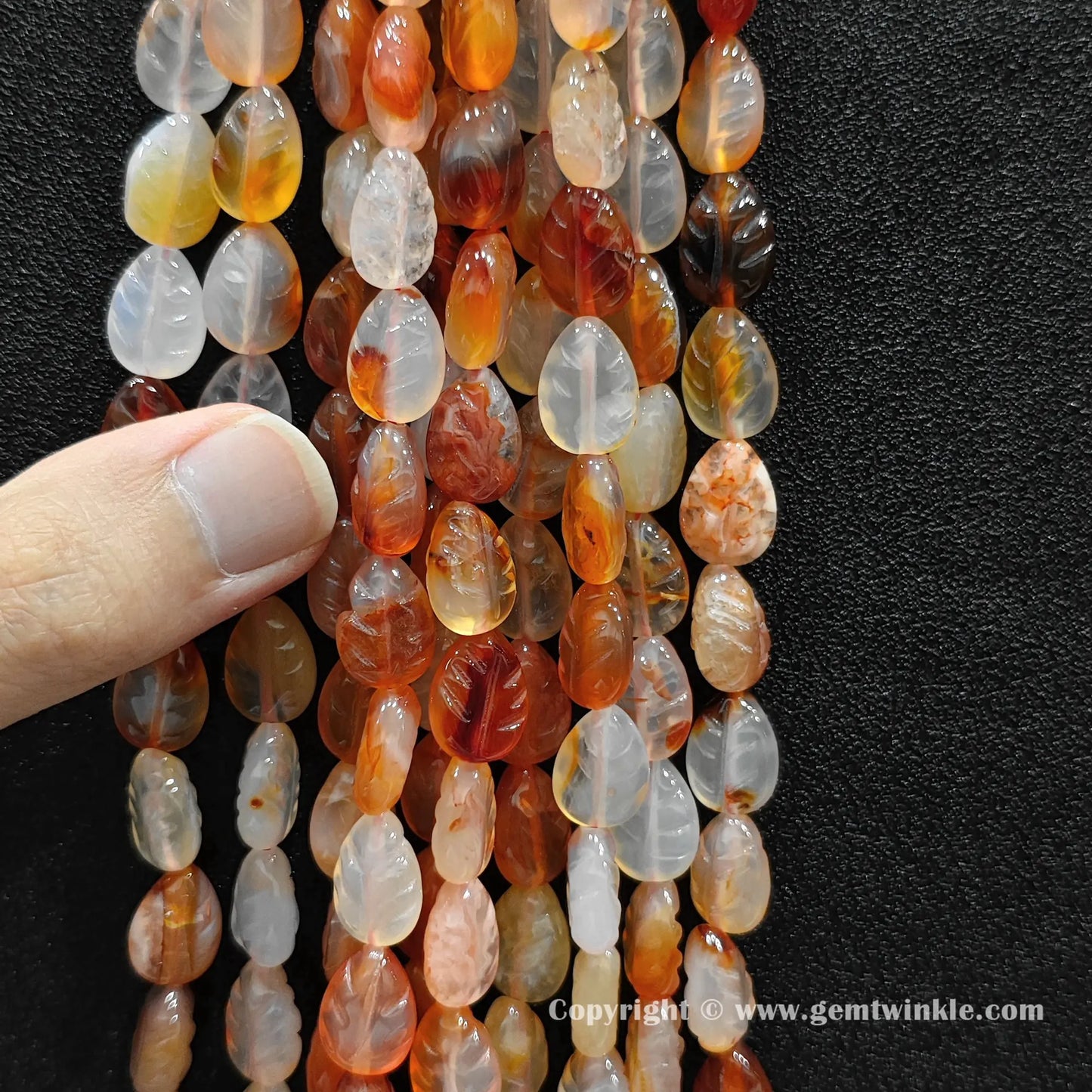 Close up view of red agate leaf carved beads held on fingers for quality preview