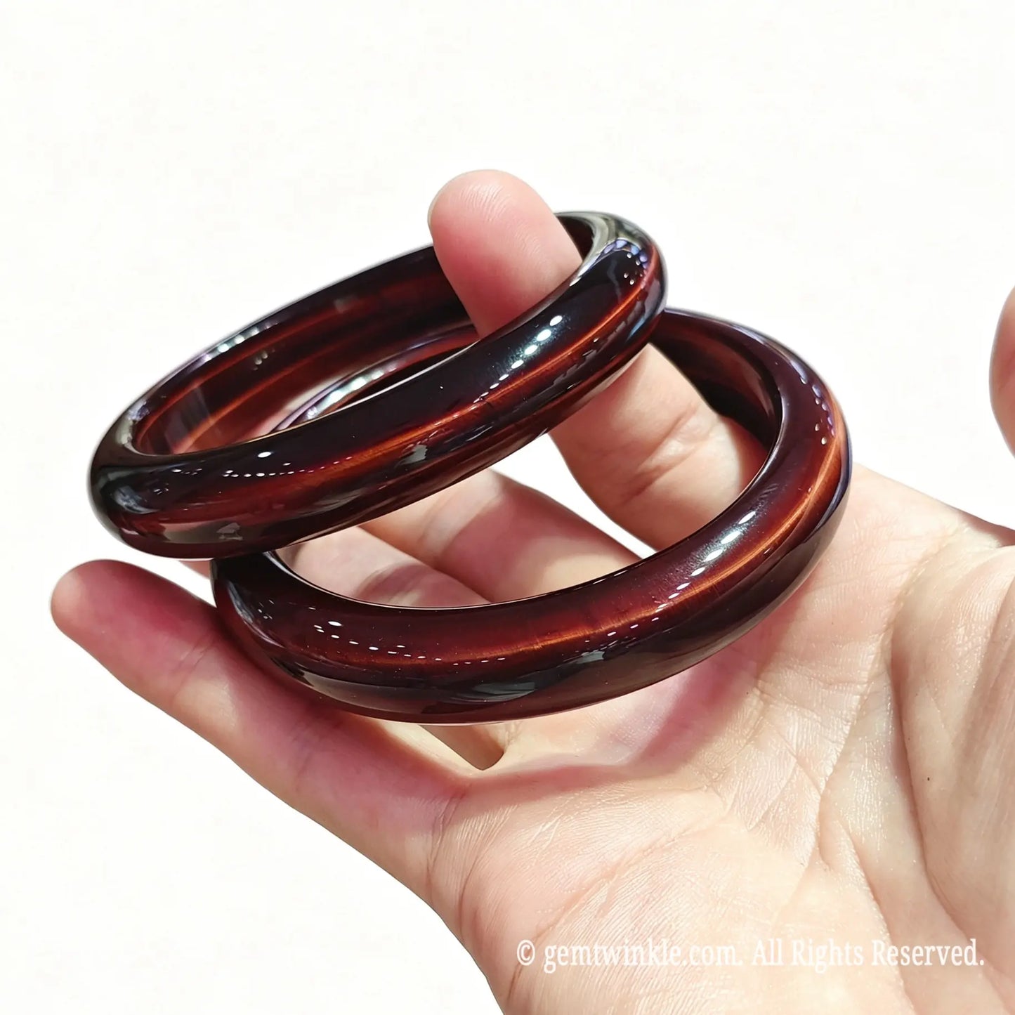 Stacked red tiger eye gemstone bangles resting on palm displaying classic round profile and glossy surface