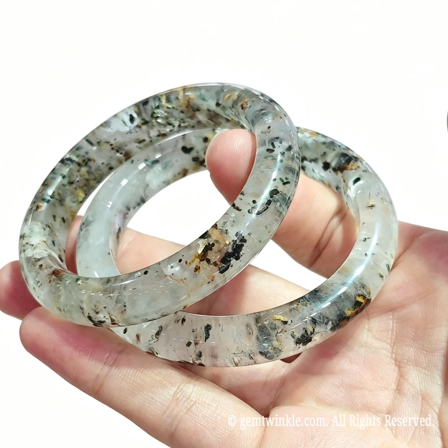 Stacked natural three lives stone quartz bangles resting on palm displaying clear crystal matrix and smooth inner ring