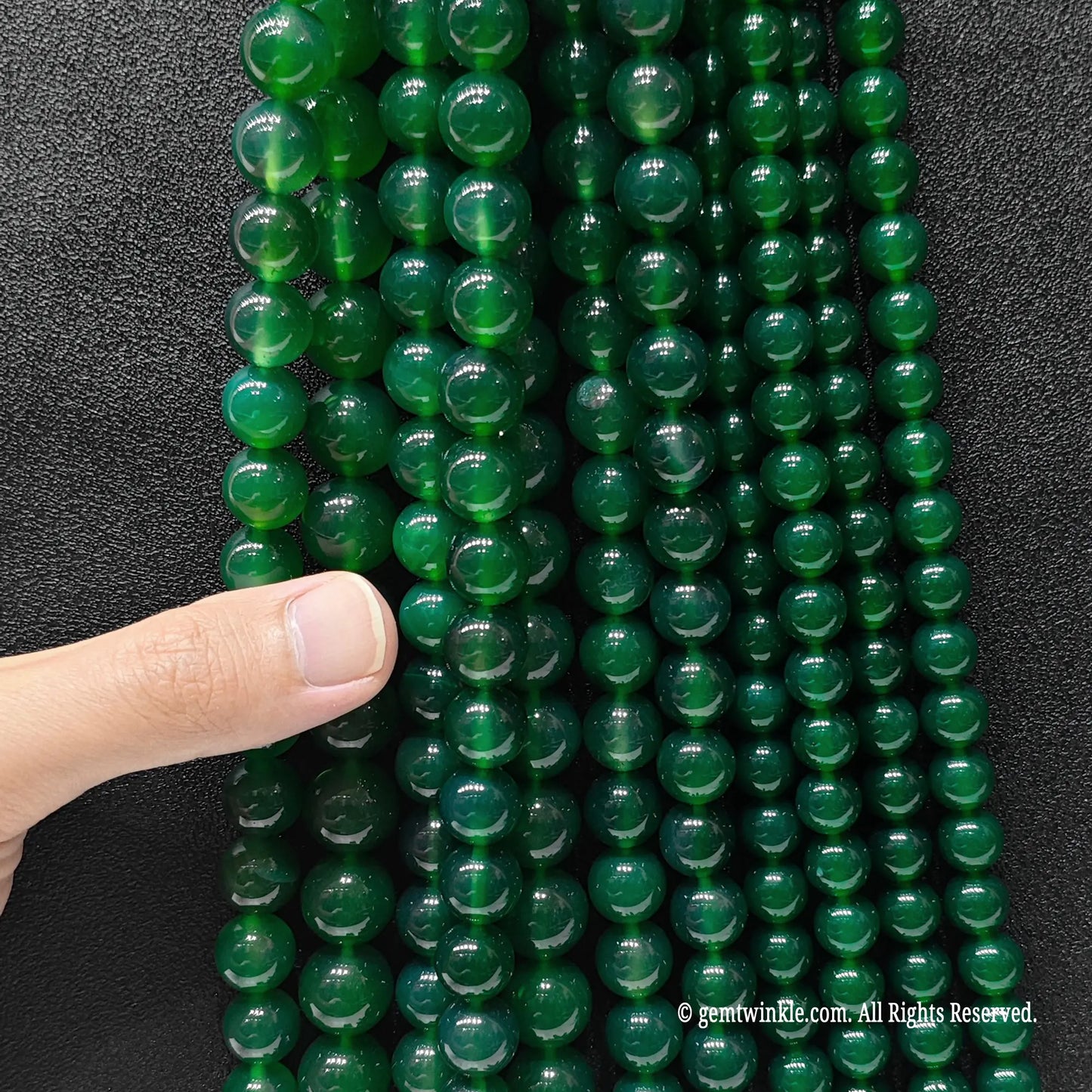 Multiple strands of green agate round beads held in hand for scale and size range verification