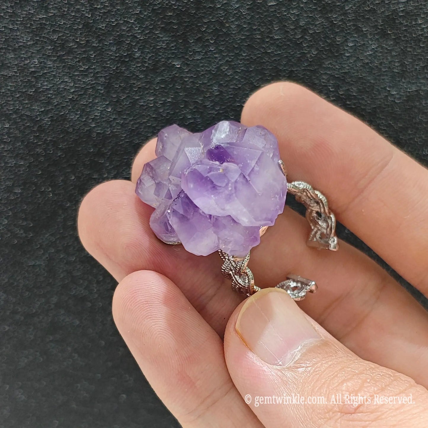 Uncut purple amethyst crystal column ring held under studio light displaying translucent violet crystal terminations
