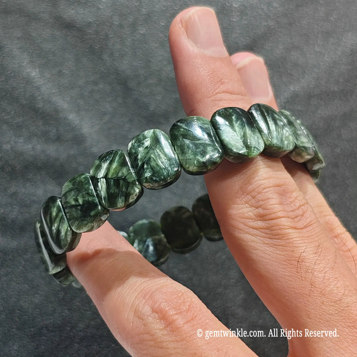 Full view of a unisex forest green seraphinite cuff held in hand showing smooth reflective surface