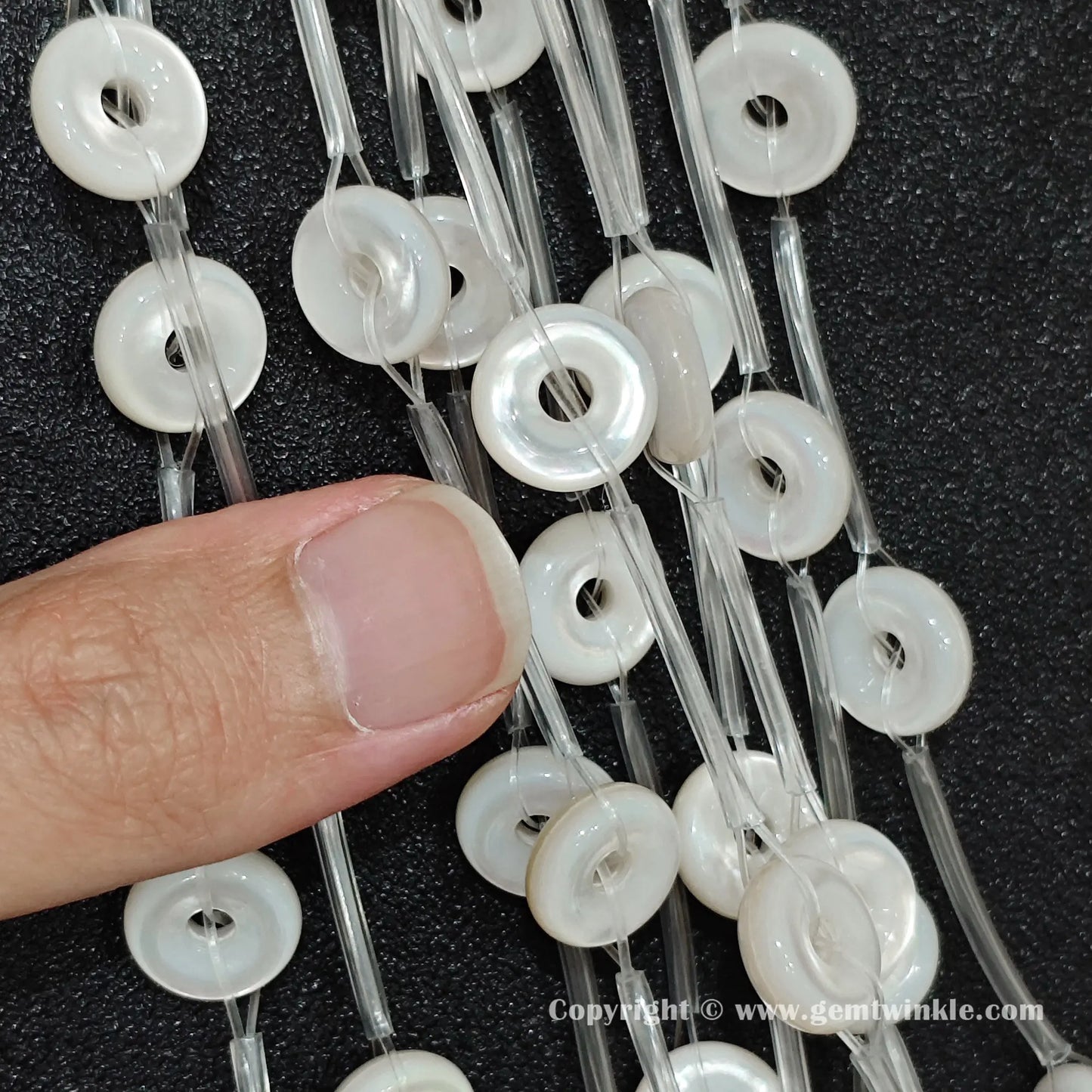 Detailed shot of white shell flat donut washer beads examined against fingertips to display luster