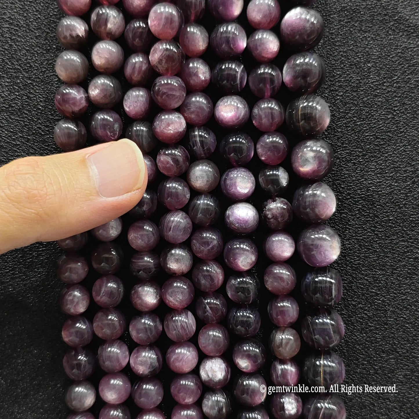 Hand inspecting a collection of purple lepidolite crystal beads strands to show size choices and quality details