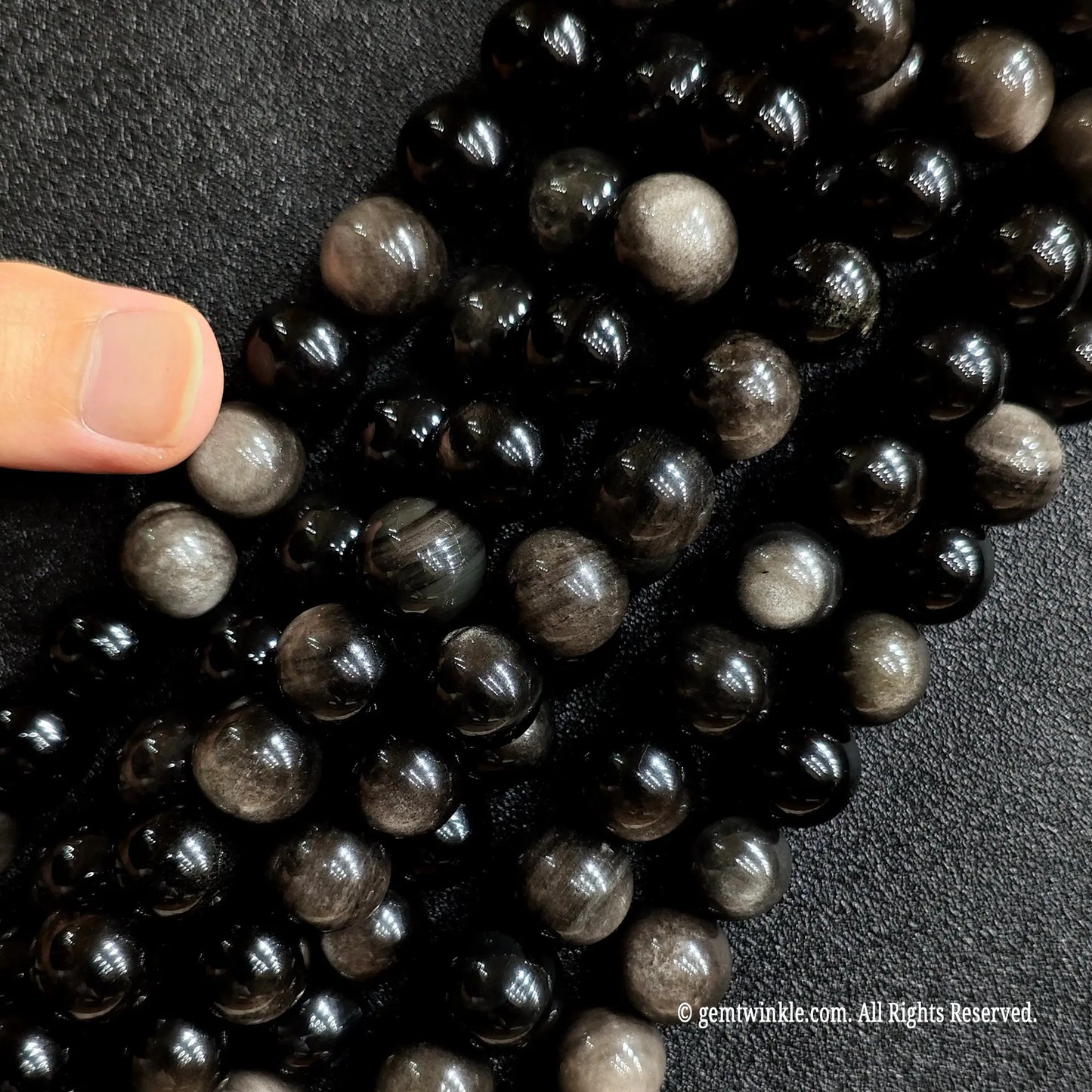 Hand holding multiple strands of natural silver sheen obsidian crystal beads to showcase size choice grid
