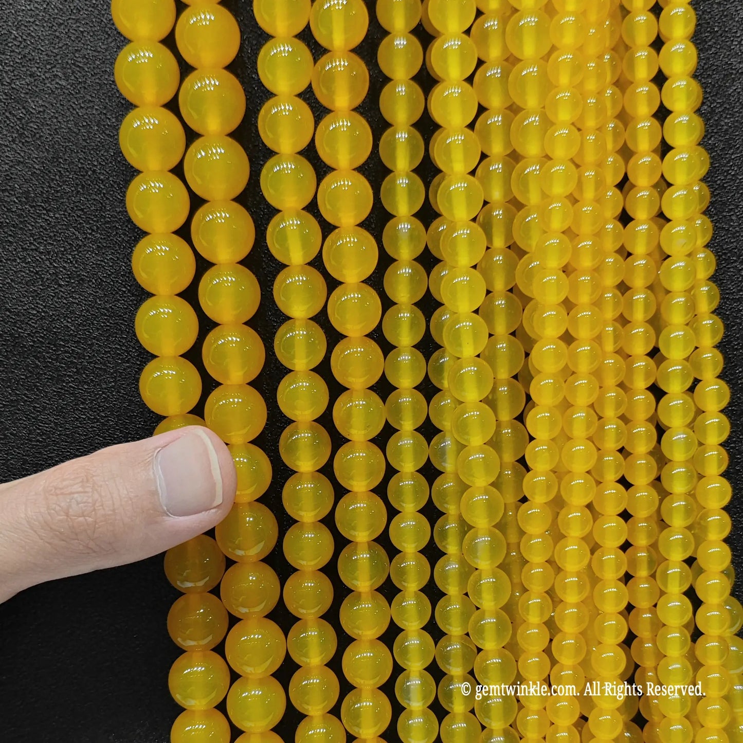 A full bunch of yellow agate round beads from 4mm to 14mm held in hand for studio stock inspection