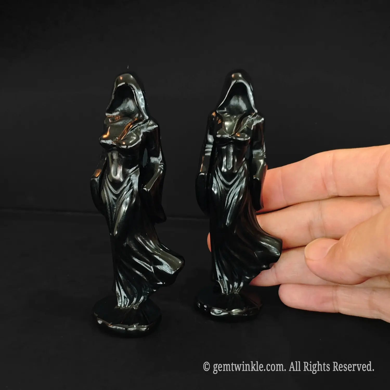 A human hand holding a 10cm black obsidian shrouded goddess statue to demonstrate the scale and high gloss polish