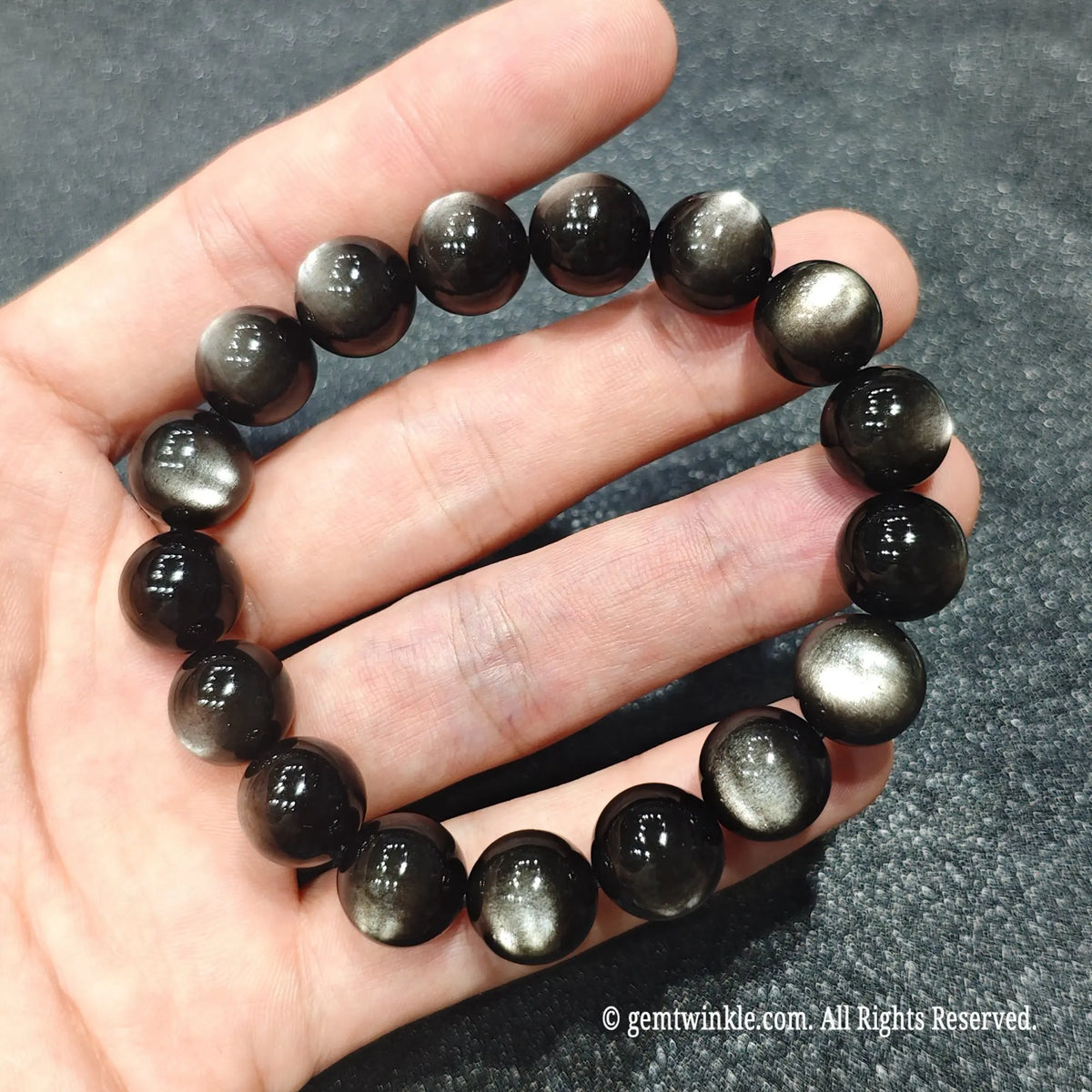 Handholding a natural silver sheen obsidian stretch bracelet showcasing smooth polished surface and strong optical depth
