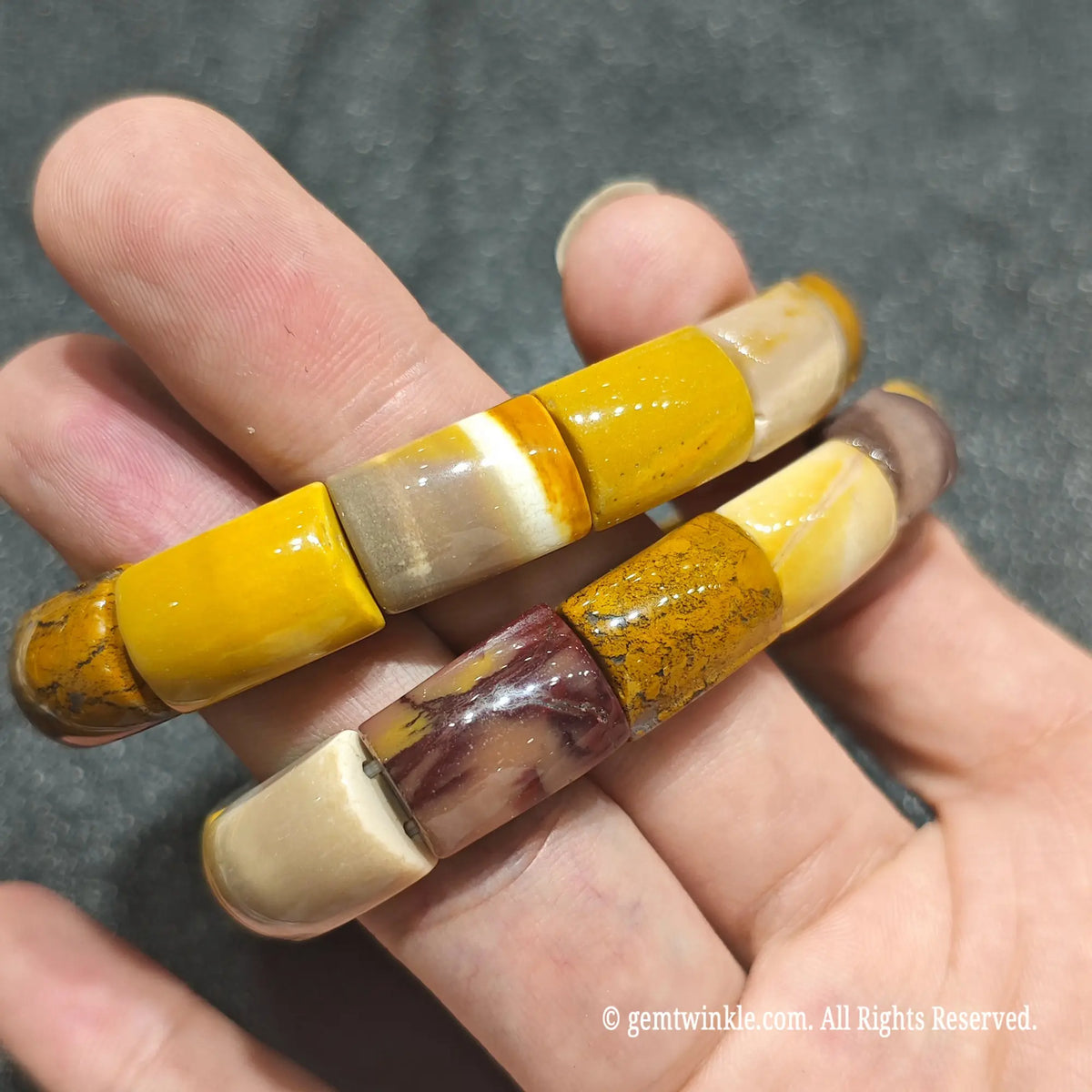 Close up view of 16mm mookaite cylinder beads held over palm showing smooth surface polish and rich yellow tones