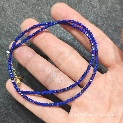 Close up of 2.5mm Lapis Lazuli square beads looped on hand highlighting gold-plated lobster clasp and extender