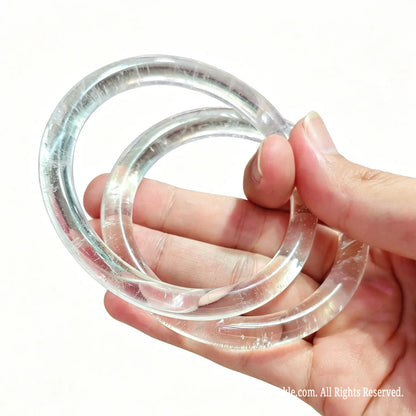 Two natural clear quartz slim bangles held together highlighting pure crystal structure under light