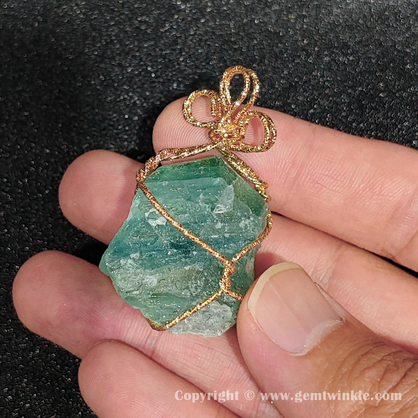 Handheld view of 30mm green fluorite rough wire wrapped pendant showing translucent mint tone