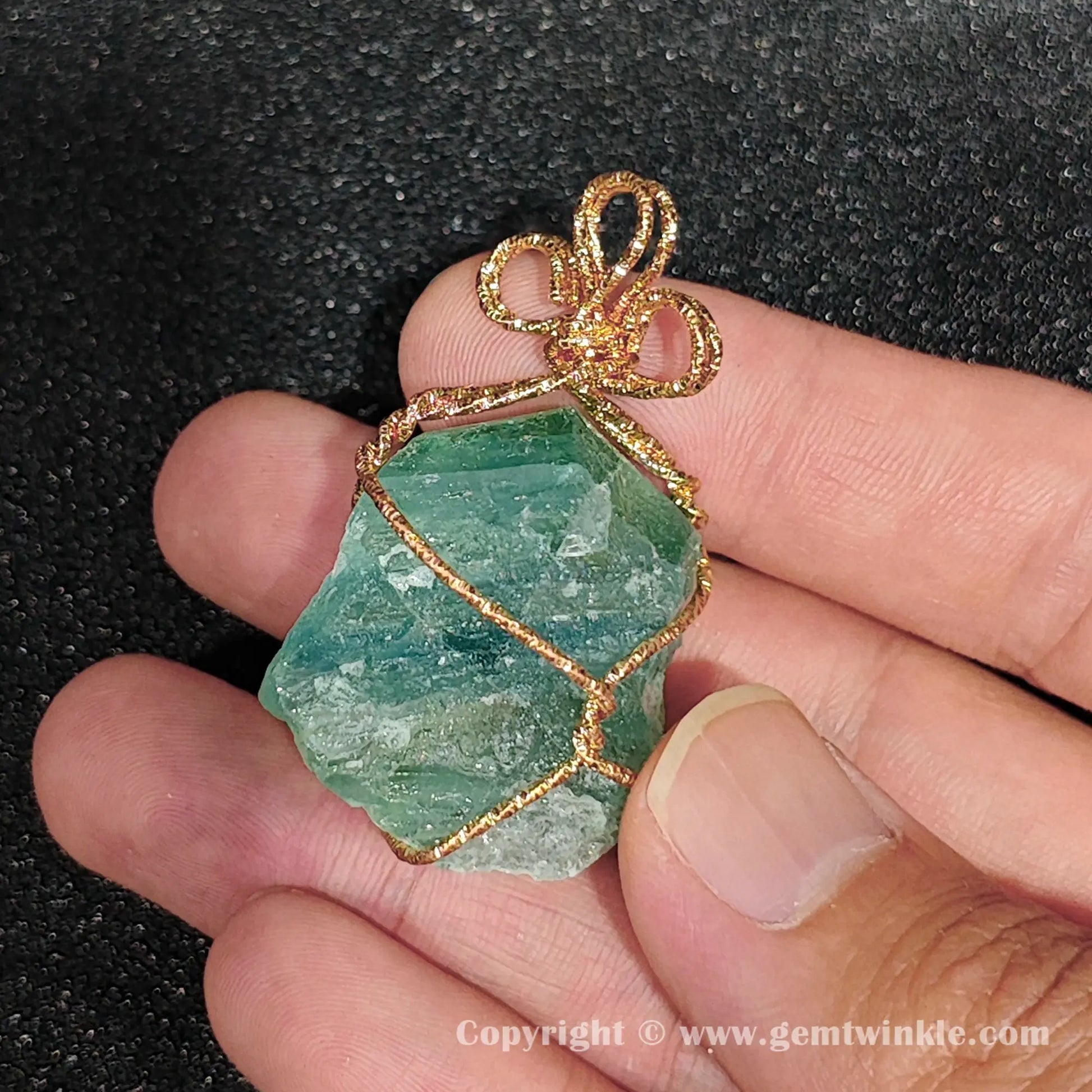 Handheld view of 30mm green fluorite rough wire wrapped pendant showing translucent mint tone