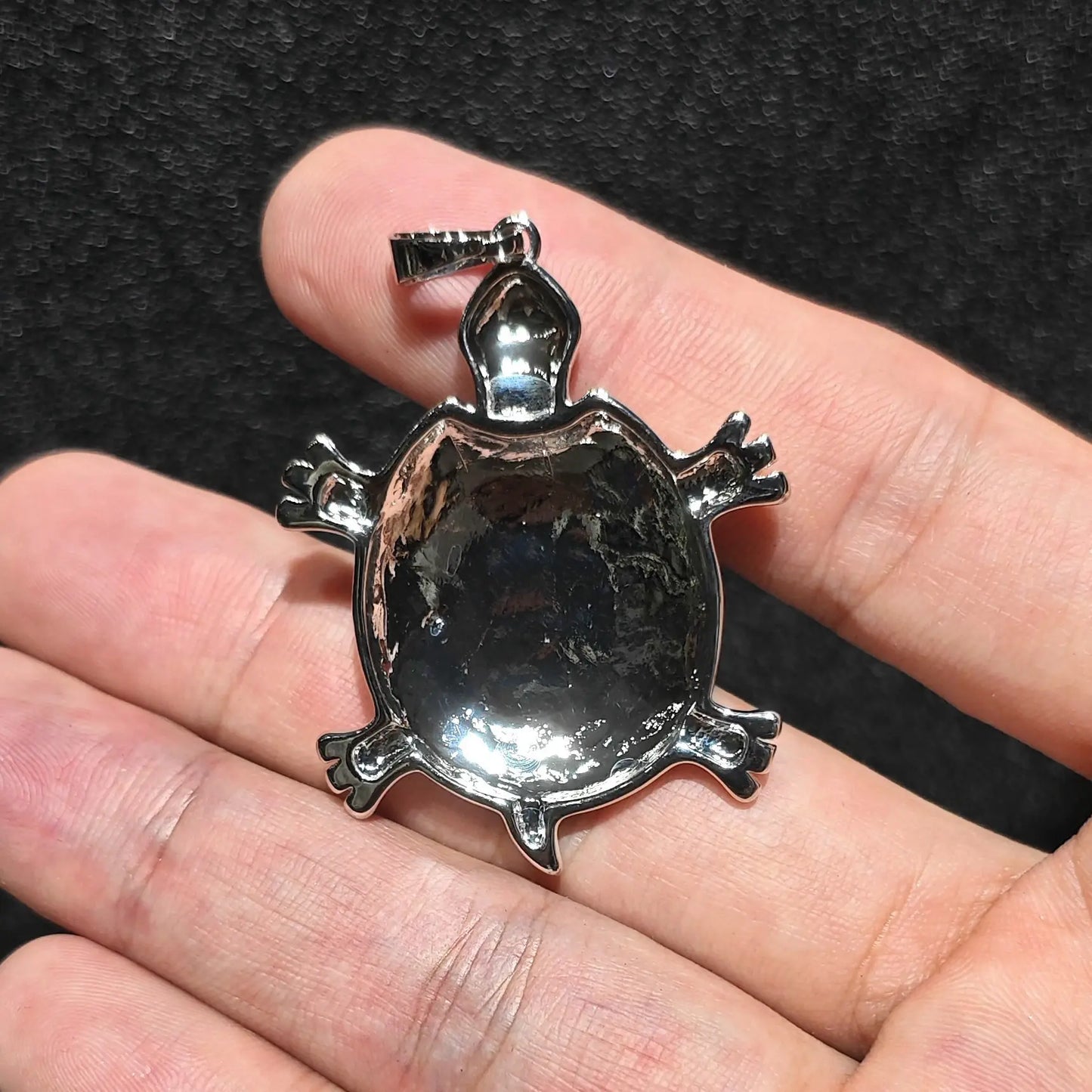 Back view comparison of 35mm sea turtle pendant showing silver tone alloy metal backing and bail loop held on hand